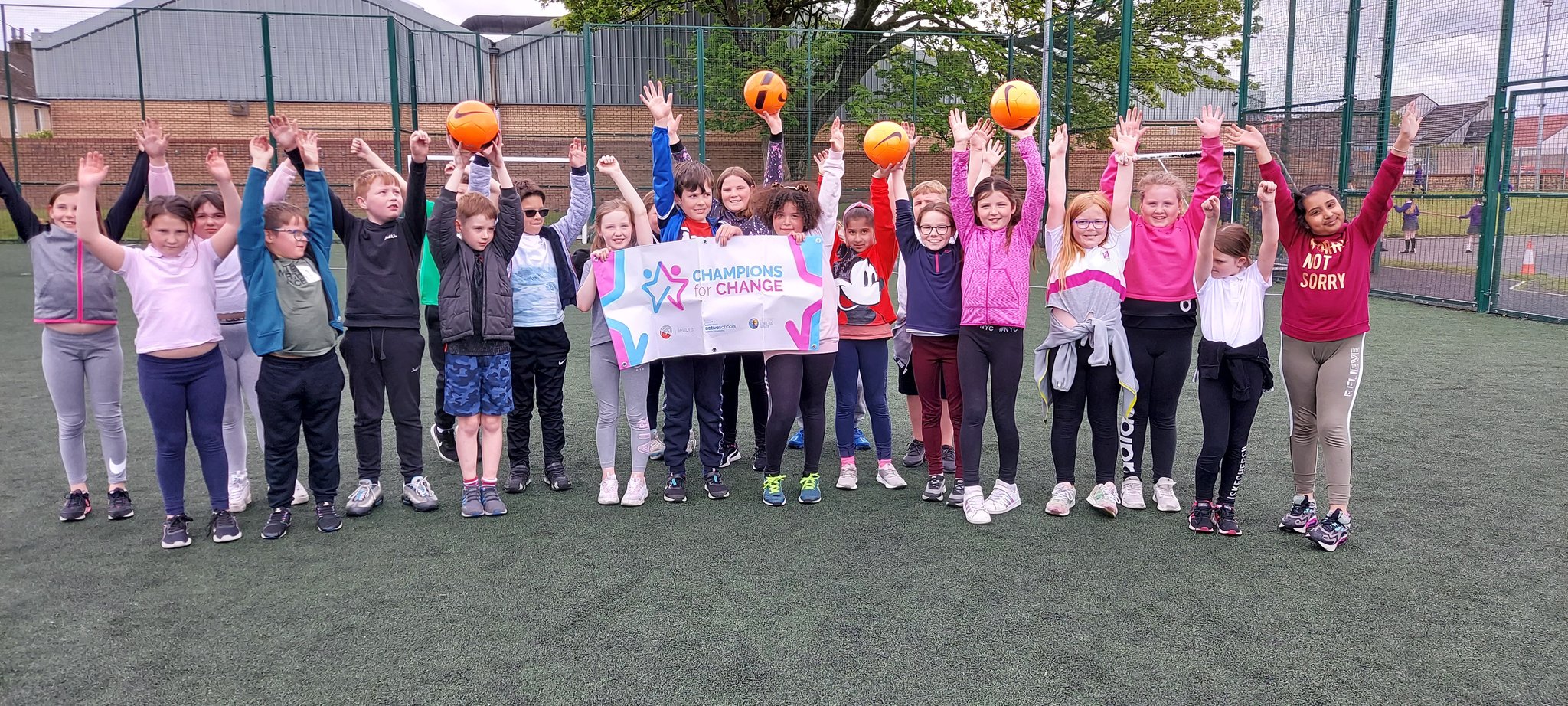 Children raise their hands in the air on a football pitch.