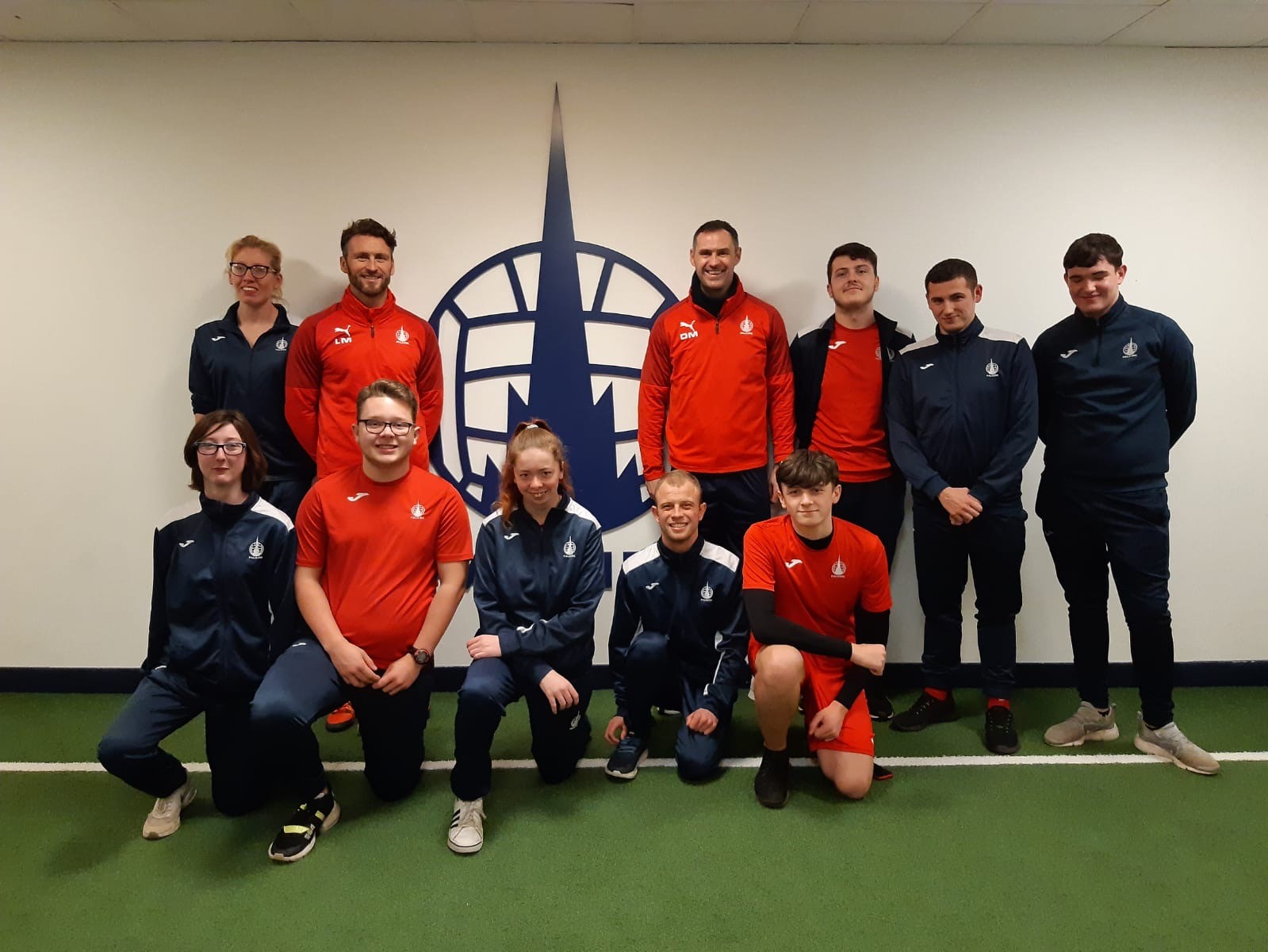 Group of people from a sports club posing for a picture in front of their club logo.
